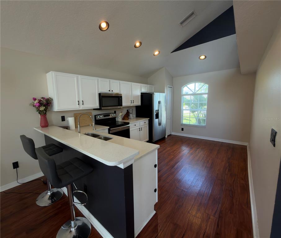 A kitchen with white cabinets, stainless steel appliances, a breakfast bar, and dark wood flooring — 8103 TAR HOLLOW DRIVE, GIBSONTON, FL