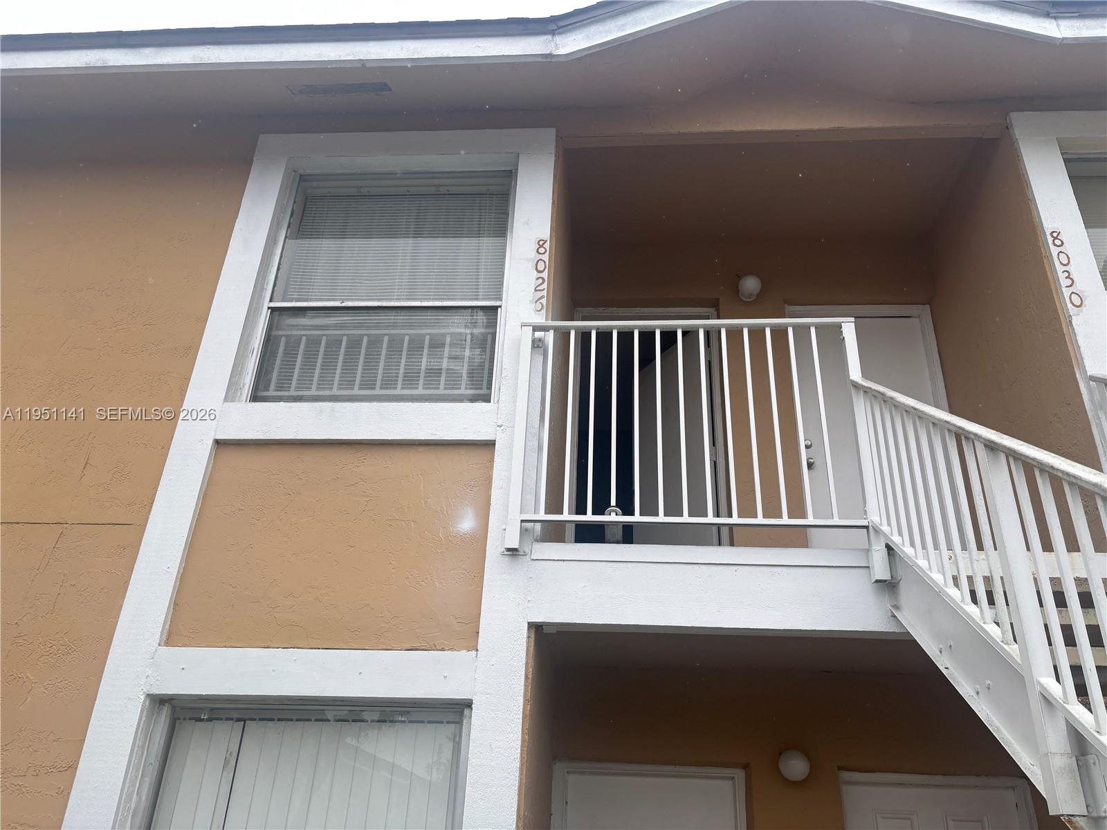 The exterior of a two-story apartment building features tan stucco walls, white trim, and metal staircases — 8026 SW 21st Ct # 8026, Miramar FL 33025, MIRAMAR, FL