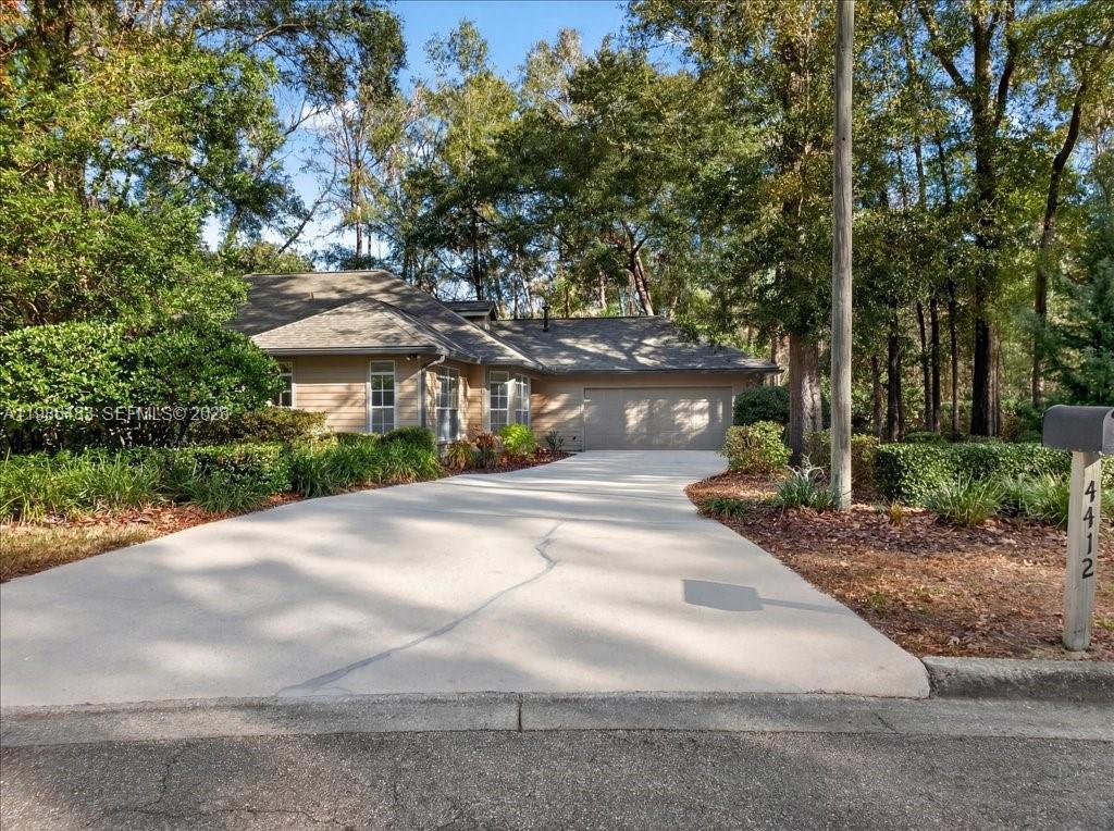A tan house with a concrete driveway and a two-car garage sits among trees — 4412 SW 101st Dr, Gainesville FL 32608, GAINESVILLE, FL