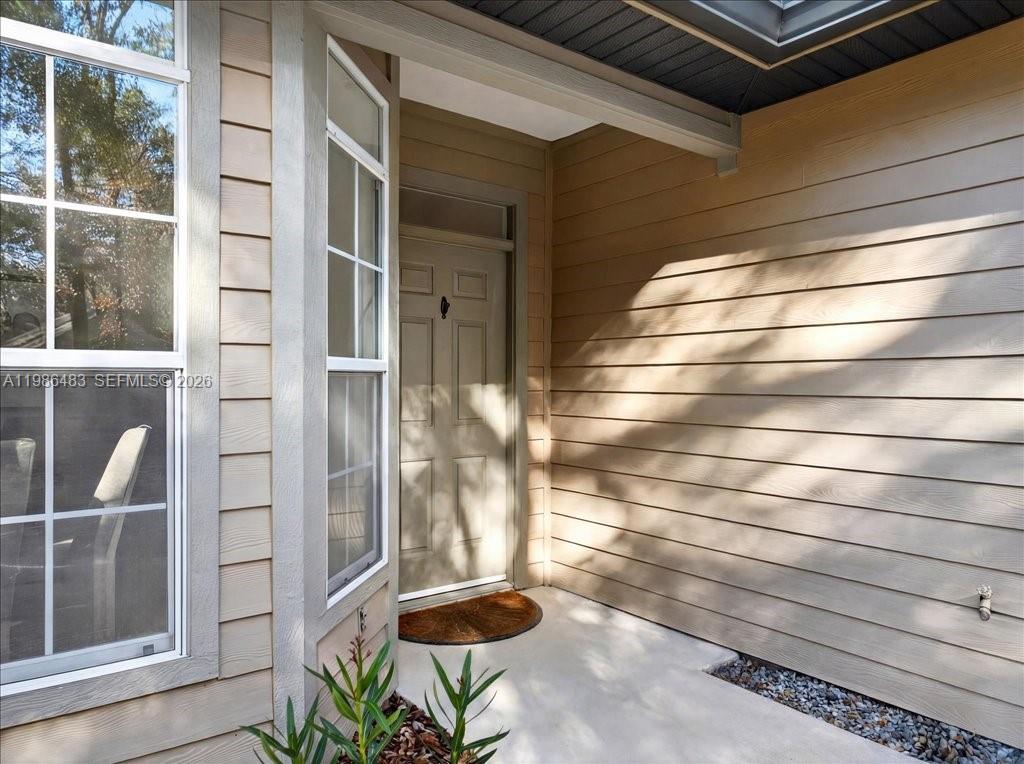 A beige front door with a transom window sits under a covered entryway with siding — 4412 SW 101st Dr, Gainesville FL 32608, GAINESVILLE, FL