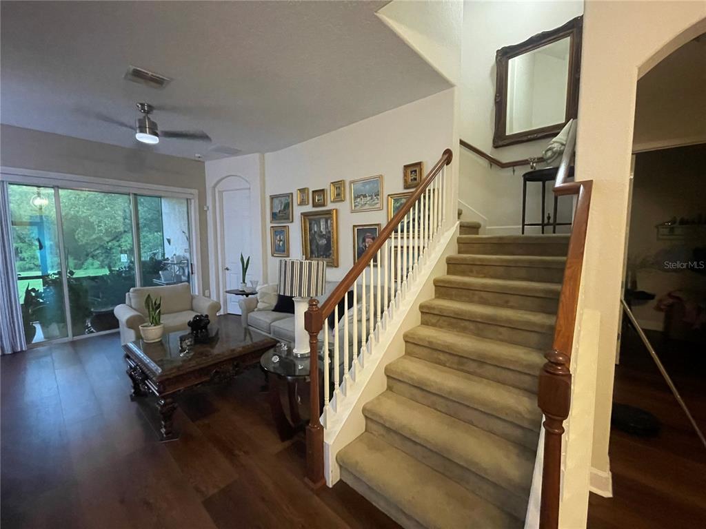 A living room features wood flooring, a carpeted staircase, and a gallery wall of framed art — 2821 PLYMOUTH PLACE, KISSIMMEE, FL