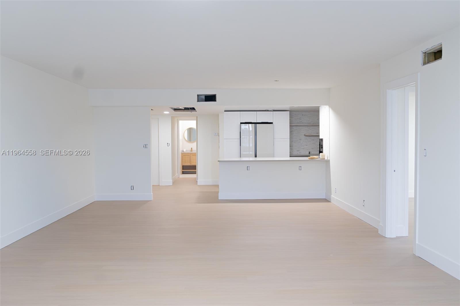 A bright, minimalist living area features light wood flooring, white walls, and an open kitchen — 3051 N Course Dr # 107, Pompano Beach FL 33069, POMPANO BEACH, FL