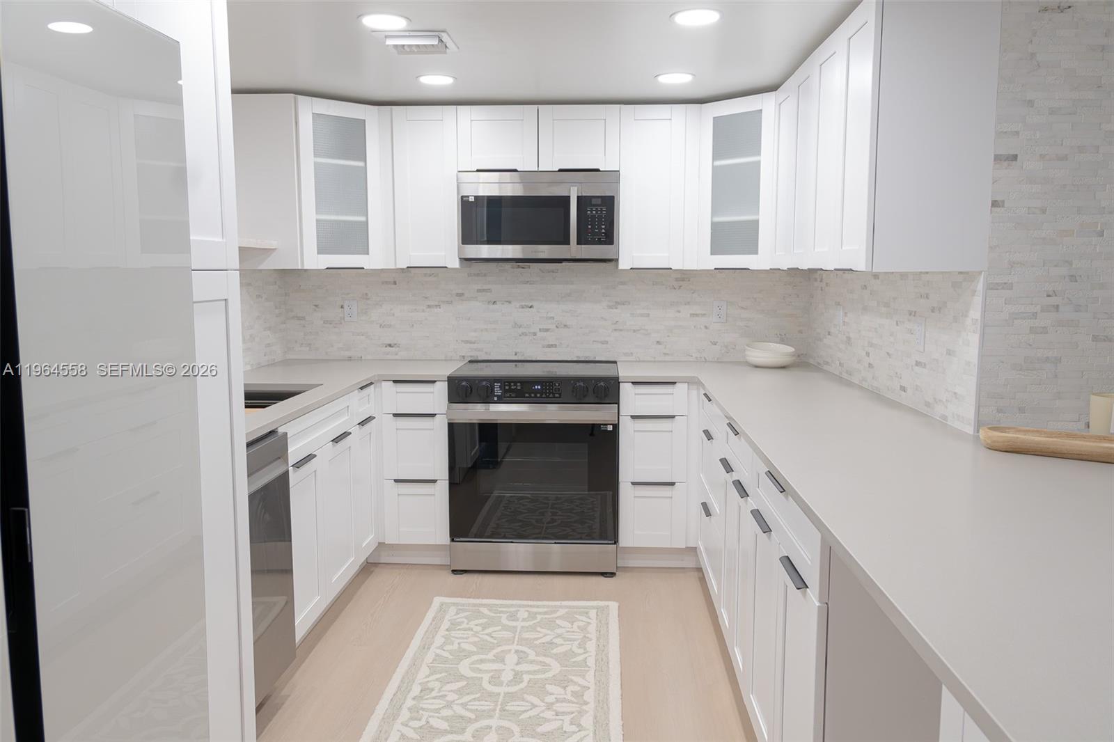 A modern kitchen features white cabinets, stainless steel appliances, and light gray countertops — 3051 N Course Dr # 107, Pompano Beach FL 33069, POMPANO BEACH, FL