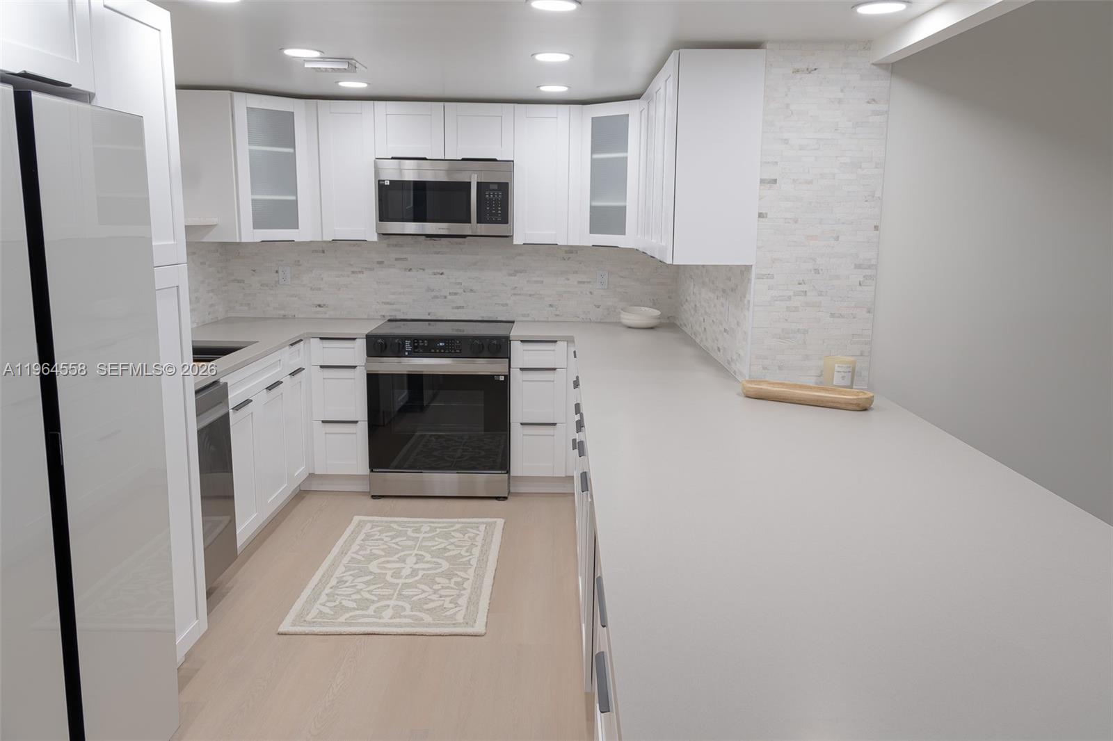 A modern kitchen features white cabinets, stainless steel appliances, and light gray countertops — 3051 N Course Dr # 107, Pompano Beach FL 33069, POMPANO BEACH, FL