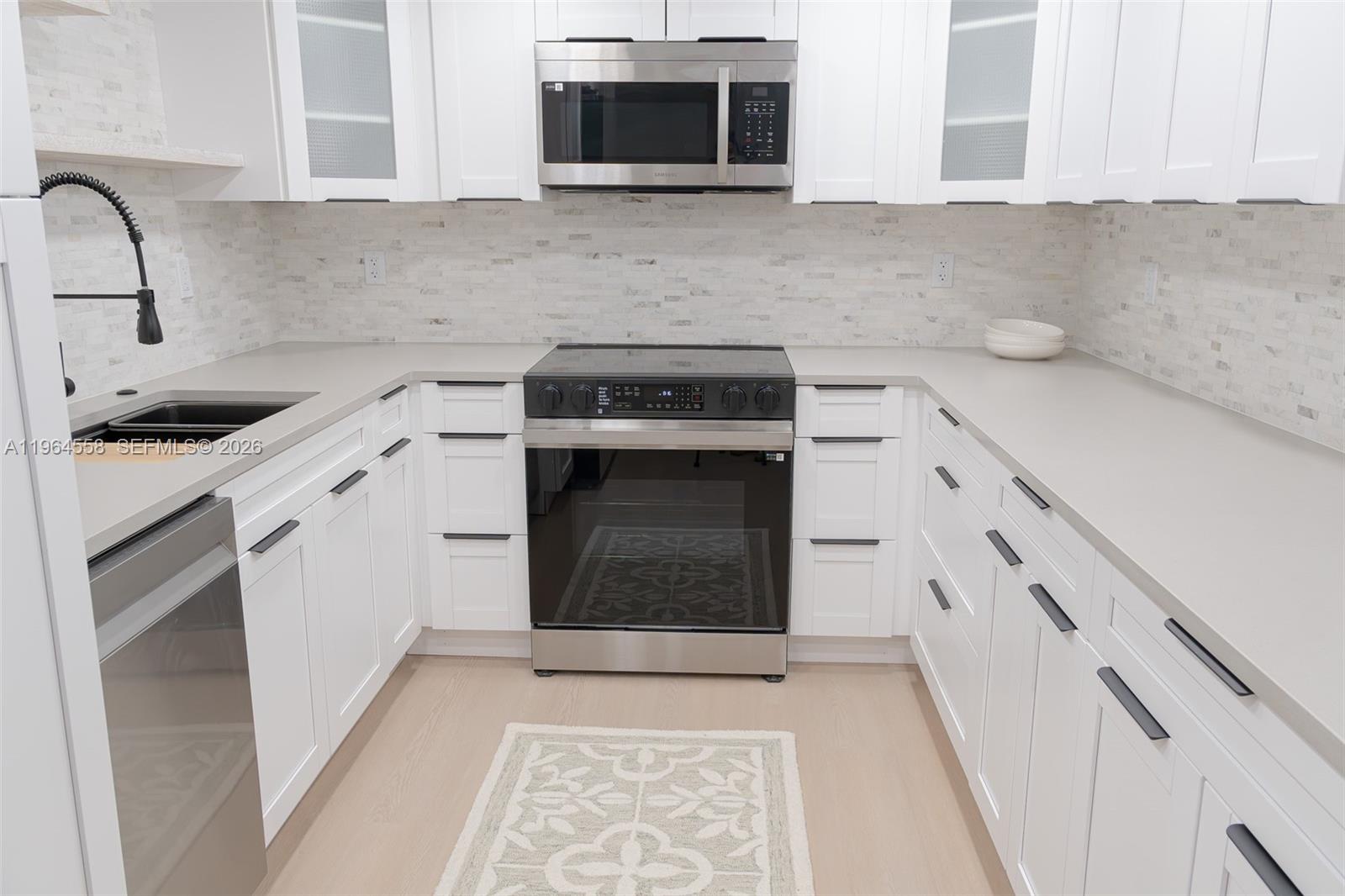 A modern kitchen features white cabinetry, stainless steel appliances, and light-colored countertops — 3051 N Course Dr # 107, Pompano Beach FL 33069, POMPANO BEACH, FL