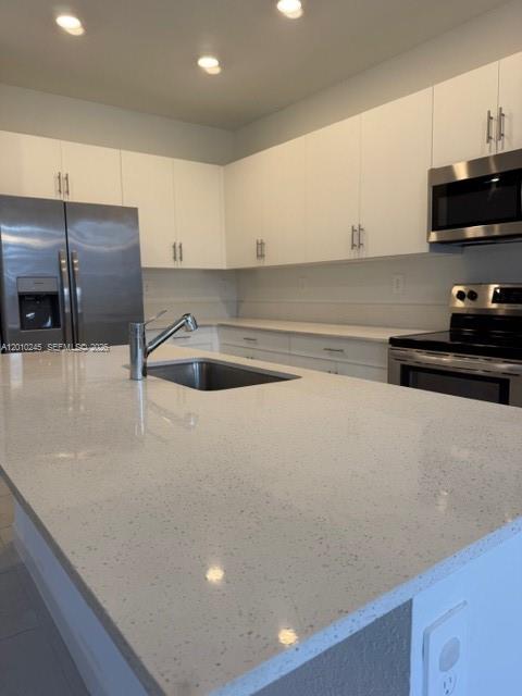 A modern kitchen features white cabinets, stainless steel appliances, and a white quartz island countertop — HOMESTEAD, FL