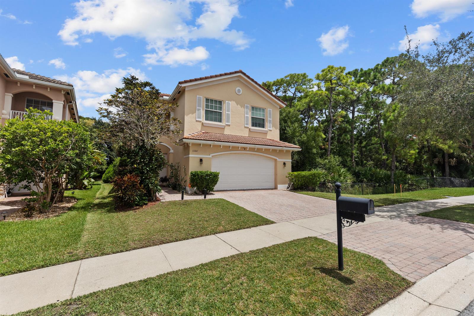 A two-story tan house with a tiled roof and a paved driveway sits on a lawn — 1104 NW Leonardo Circle, FL 34986, FL