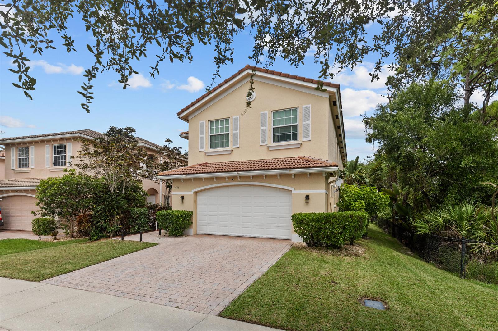 A two-story tan house with a tiled roof, white garage door, and a brick driveway — 1104 NW Leonardo Circle, FL 34986, FL