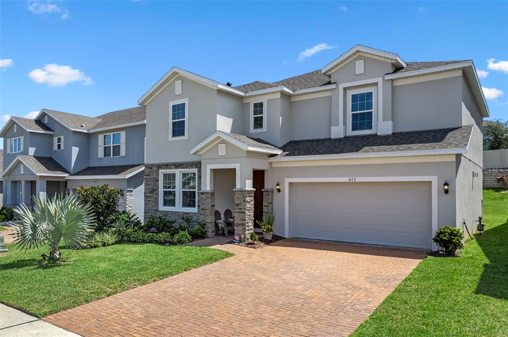 A two-story house with a beige stucco exterior, stone accents, and a brick paver driveway — 673 BLACKSTONE STREET, MINNEOLA, FL