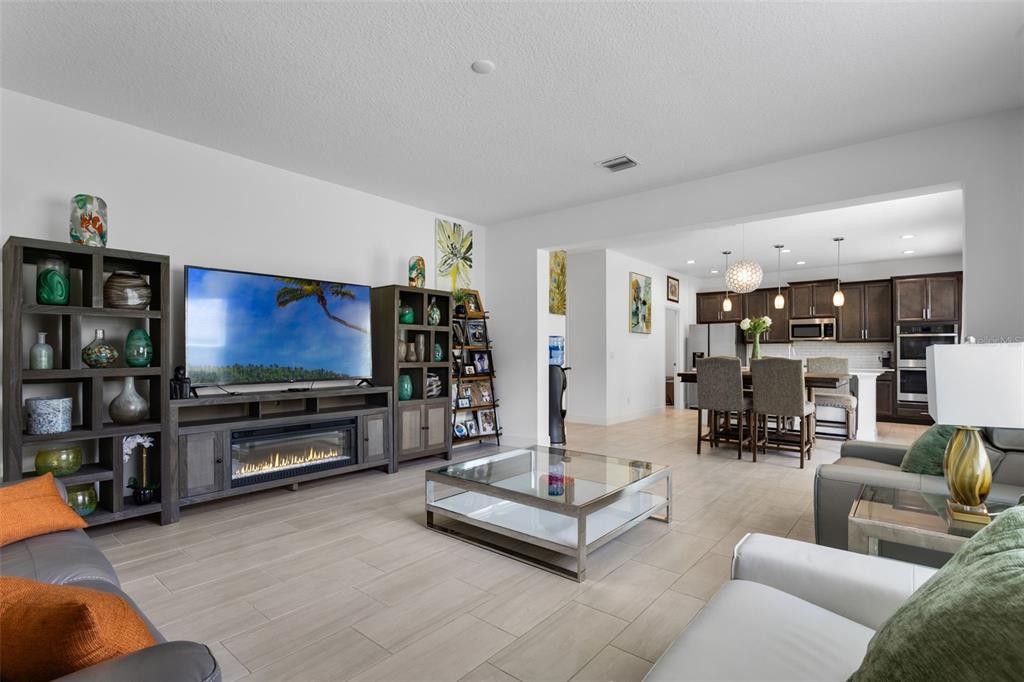 A living room with a television console, glass coffee table, and an open kitchen beyond — 673 BLACKSTONE STREET, MINNEOLA, FL
