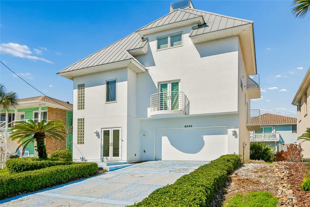 A three-story white house with a metal roof, a balcony, and a two-car garage — 6340 ENGRAM ROAD, NEW SMYRNA BEACH, FL