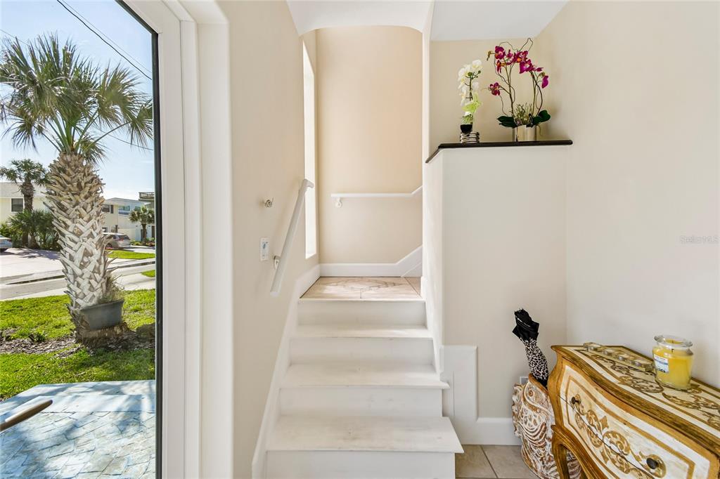 A staircase with white steps leads upward next to a glass door and entryway table — 6340 ENGRAM ROAD, NEW SMYRNA BEACH, FL
