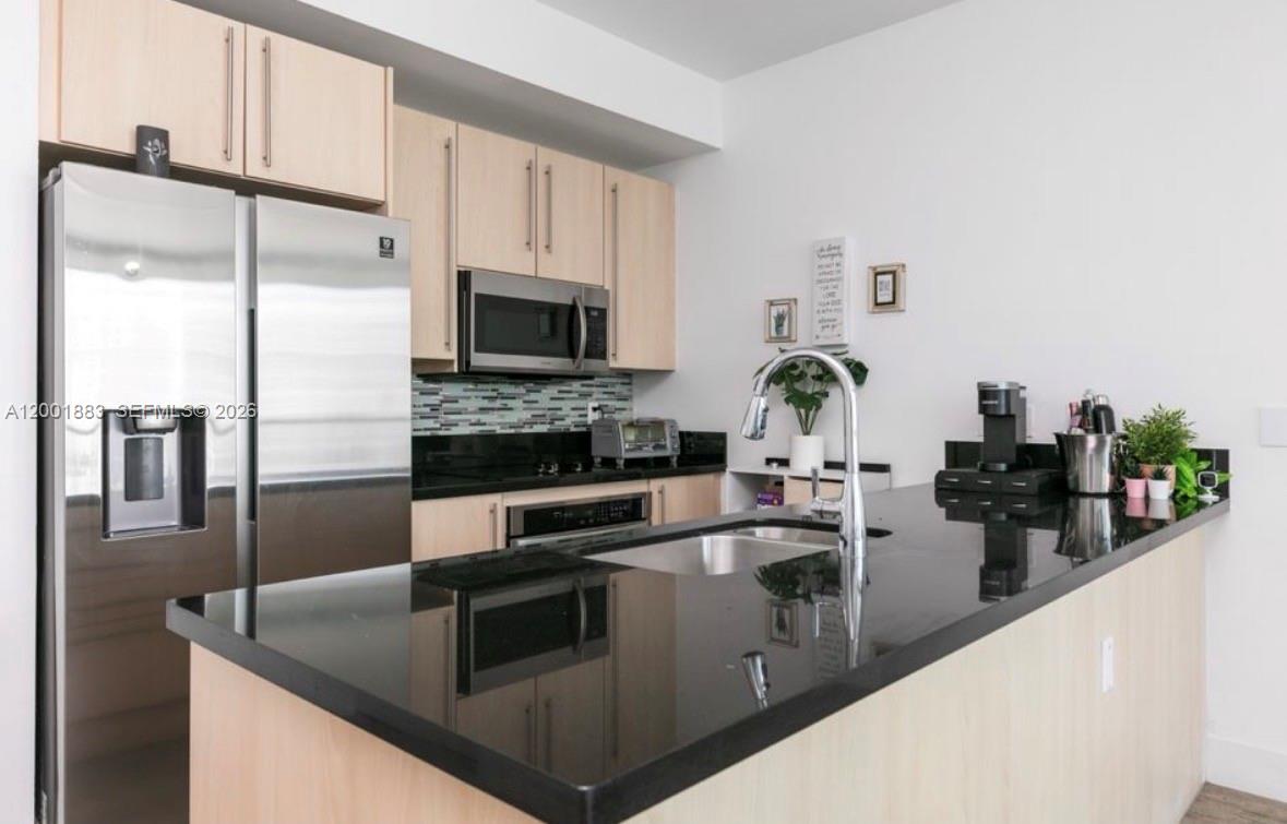 A kitchen features light wood cabinets, black countertops, stainless steel appliances, and a breakfast bar — 1111 SW 1st Ave, Miami FL 33130, MIAMI, FL