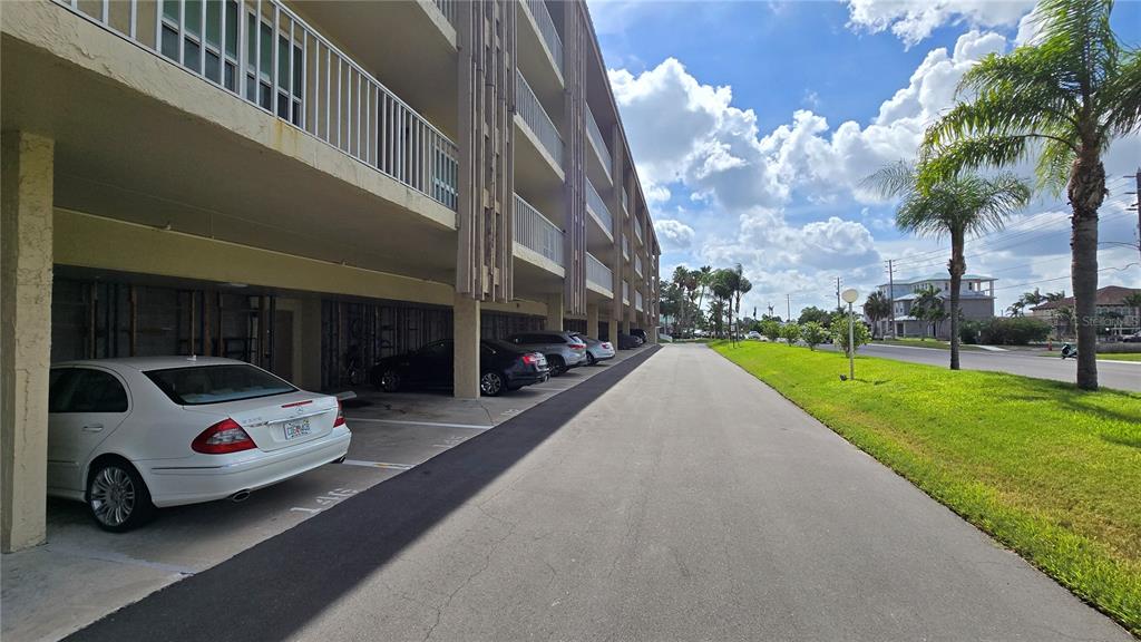 A multi-story apartment building features covered ground-level parking spaces next to a paved road — 105 ISLAND WAY UNIT 112, CLEARWATER BEACH, FL
