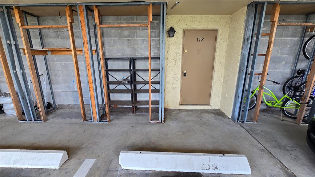 An outdoor parking space features exposed metal framing, a storage shelf, and a unit door — 105 ISLAND WAY UNIT 112, CLEARWATER BEACH, FL