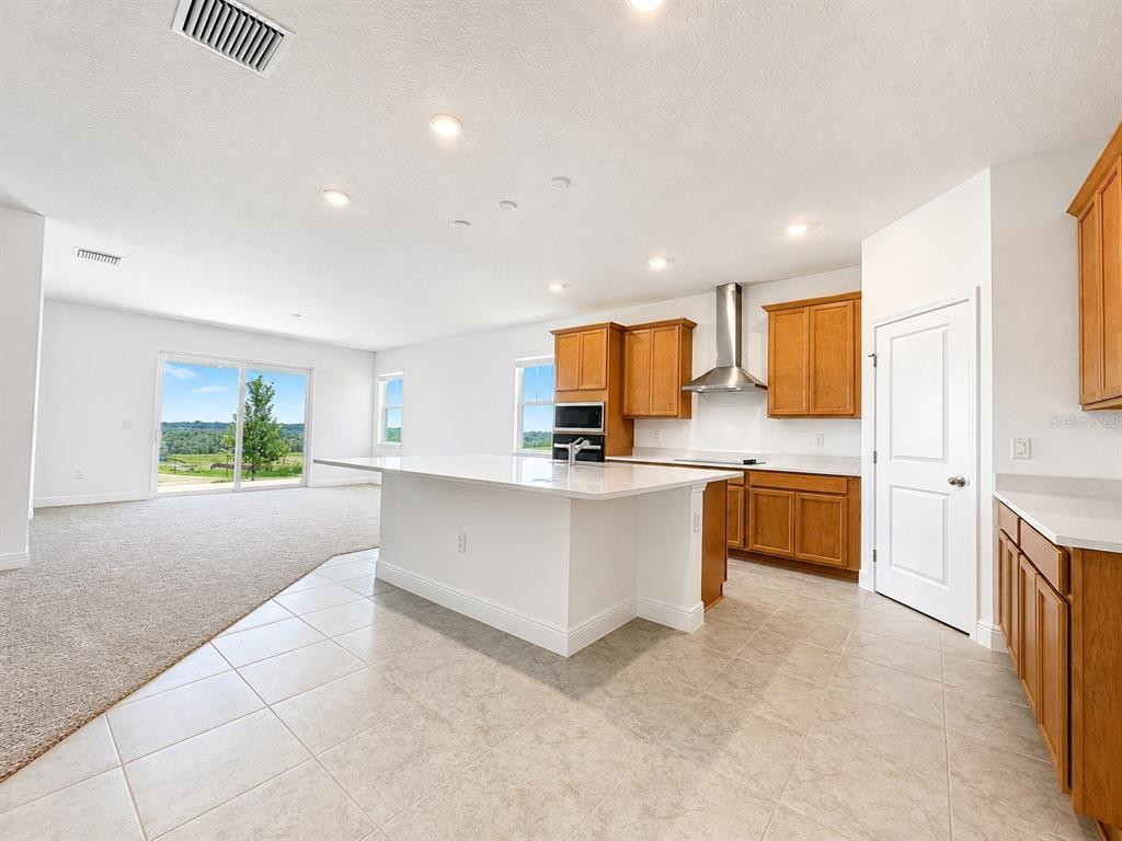 A kitchen with wood cabinets, a white island, and tile flooring opens to a carpeted living area — 2244 AXEL STREET, MINNEOLA, FL