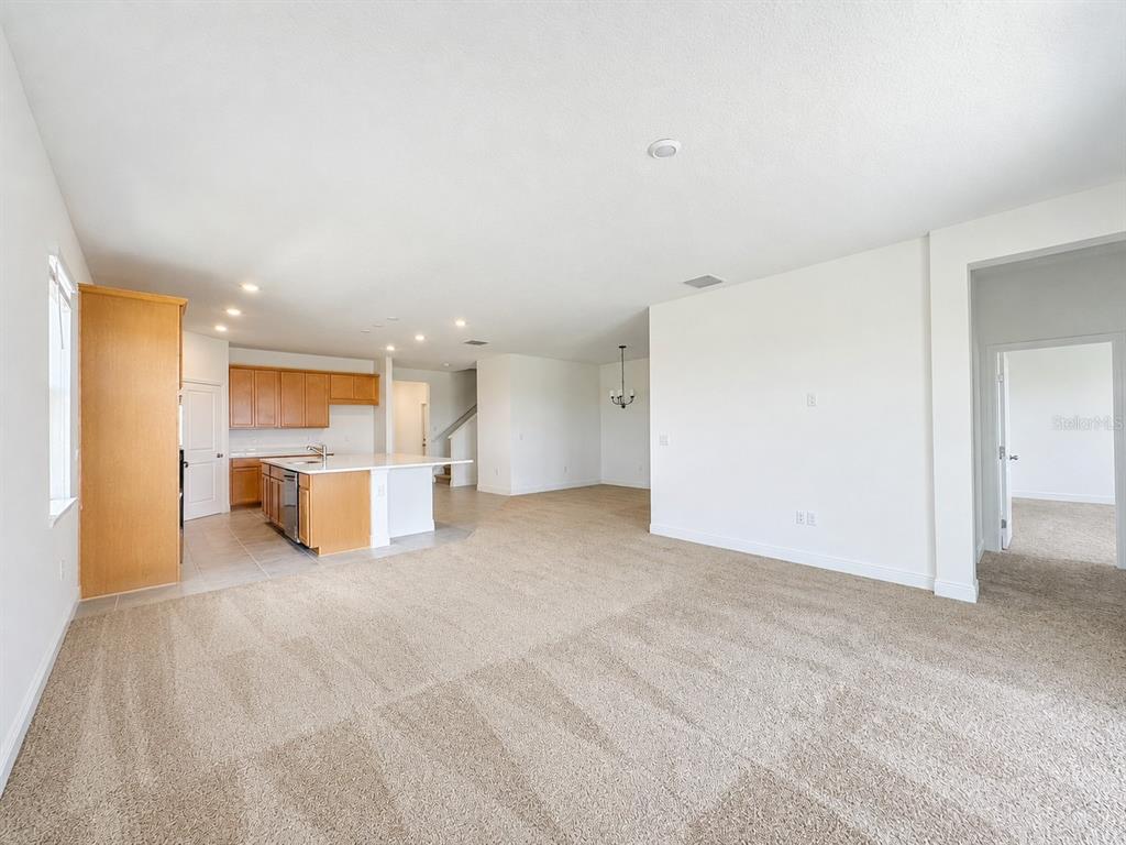 An open-concept living area features beige carpeting, a kitchen with wood cabinets, and tile flooring — 2244 AXEL STREET, MINNEOLA, FL