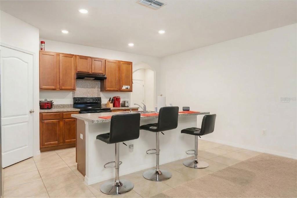 A kitchen with wood cabinets, a granite-topped island, and three black bar stools — 943 SUMMER GLEN DRIVE, WINTER HAVEN, FL