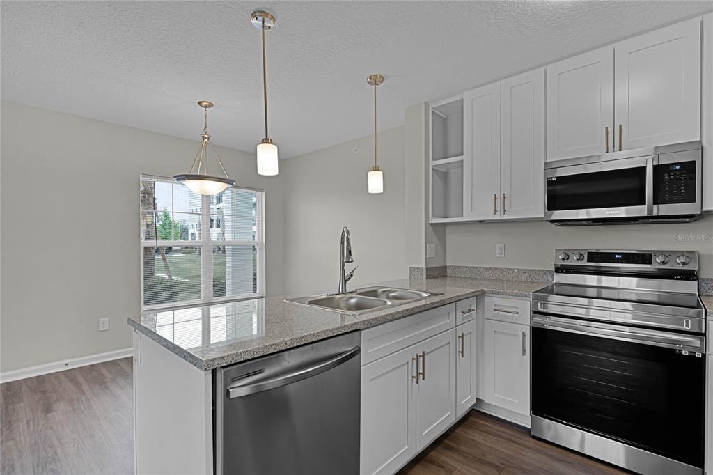 A kitchen features white cabinets, granite countertops, stainless steel appliances, and a breakfast bar — 1974 S GOLDENROD ROAD ROAD UNIT 106, ORLANDO, FL