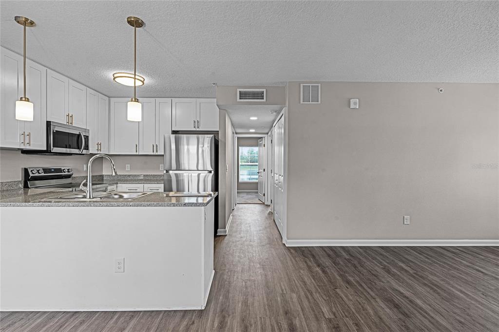 A kitchen with white cabinets and stainless steel appliances opens to a hallway and living area — 1974 S GOLDENROD ROAD ROAD UNIT 106, ORLANDO, FL
