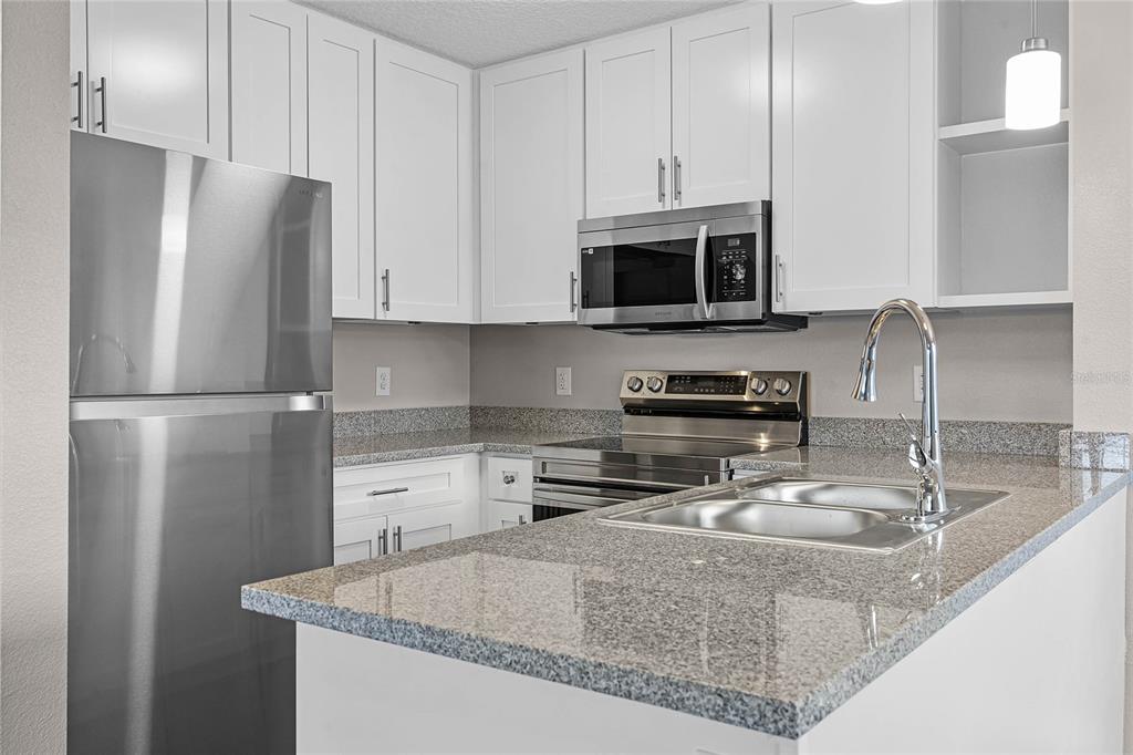A kitchen features white cabinets, granite countertops, and stainless steel appliances — 1974 S GOLDENROD ROAD ROAD UNIT 106, ORLANDO, FL