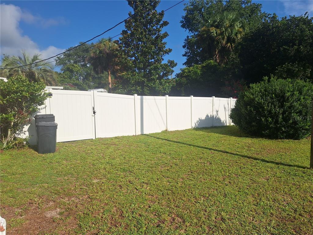 A white vinyl privacy fence encloses a grassy backyard with trees and a trash bin — 3755 SE 139TH STREET, SUMMERFIELD, FL