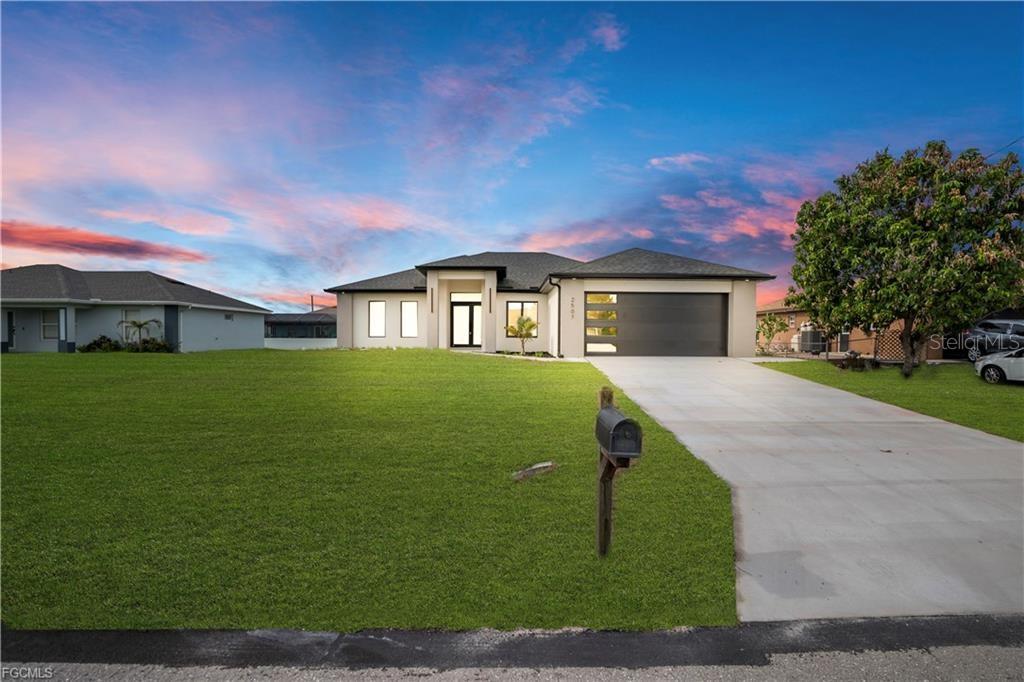 A modern single-story house with a concrete driveway and a large green lawn at sunset — 2507 39TH STREET SW, LEHIGH ACRES, FL