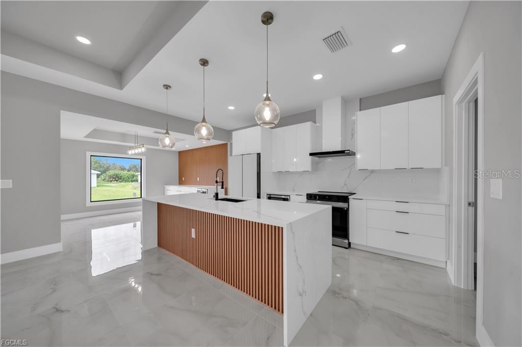 A modern kitchen features white cabinets, a marble-topped island with wood slats, and tile flooring — 2507 39TH STREET SW, LEHIGH ACRES, FL