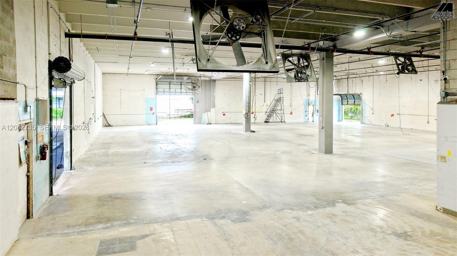An empty industrial warehouse space features concrete floors, exposed ceiling pipes, and large hanging fans — 16350 NW 48th Ave, Miami Lakes FL 33014, MIAMI LAKES, FL
