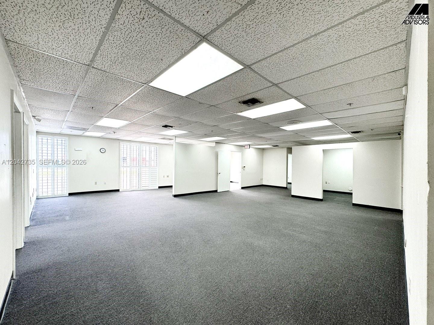 An empty office space features gray carpeting, a drop ceiling with recessed lighting, and windows — 16350 NW 48th Ave, Miami Lakes FL 33014, MIAMI LAKES, FL