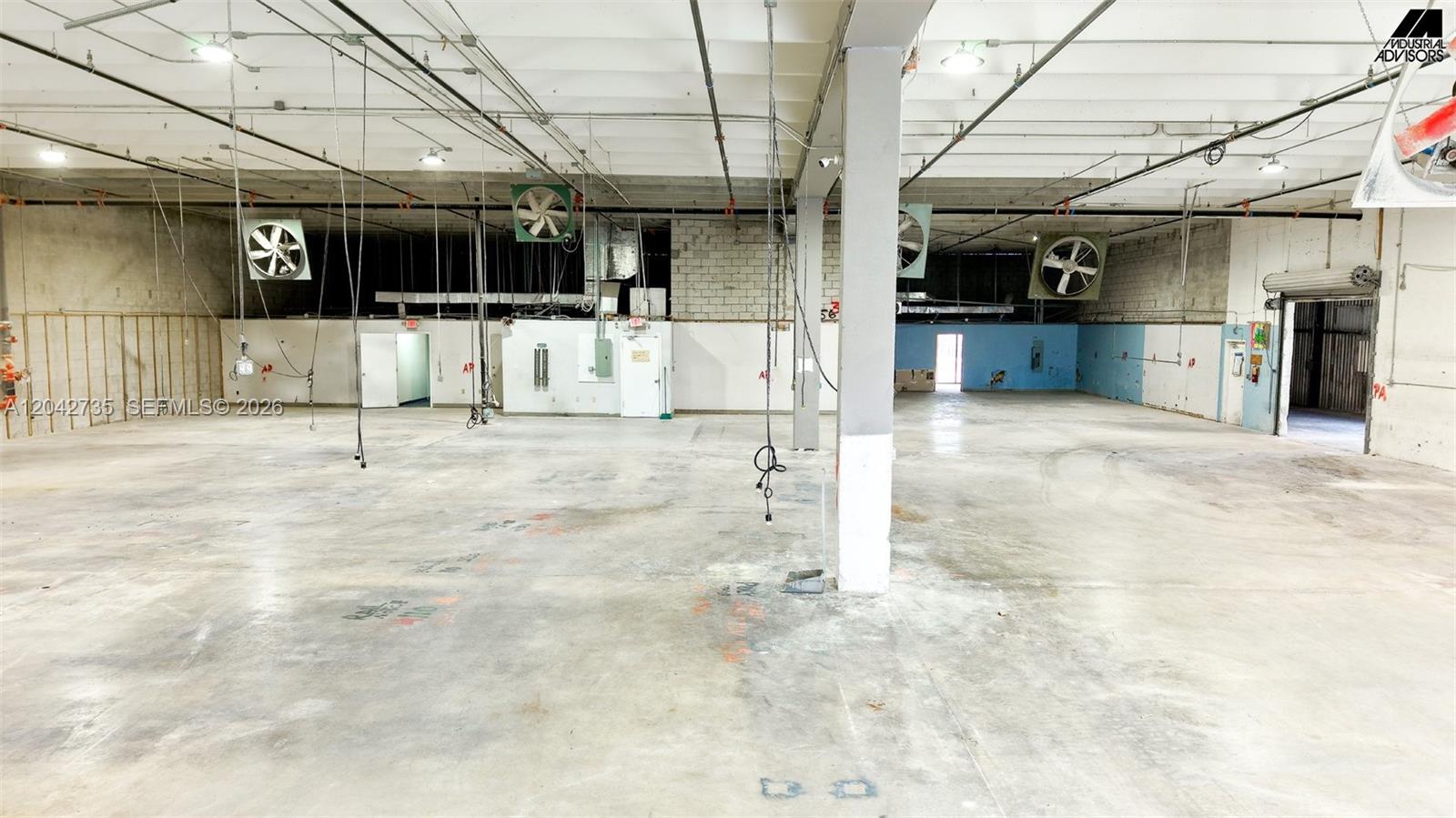 An empty industrial warehouse space features concrete floors, exposed ceiling utilities, and wall-mounted exhaust fans — 16350 NW 48th Ave, Miami Lakes FL 33014, MIAMI LAKES, FL