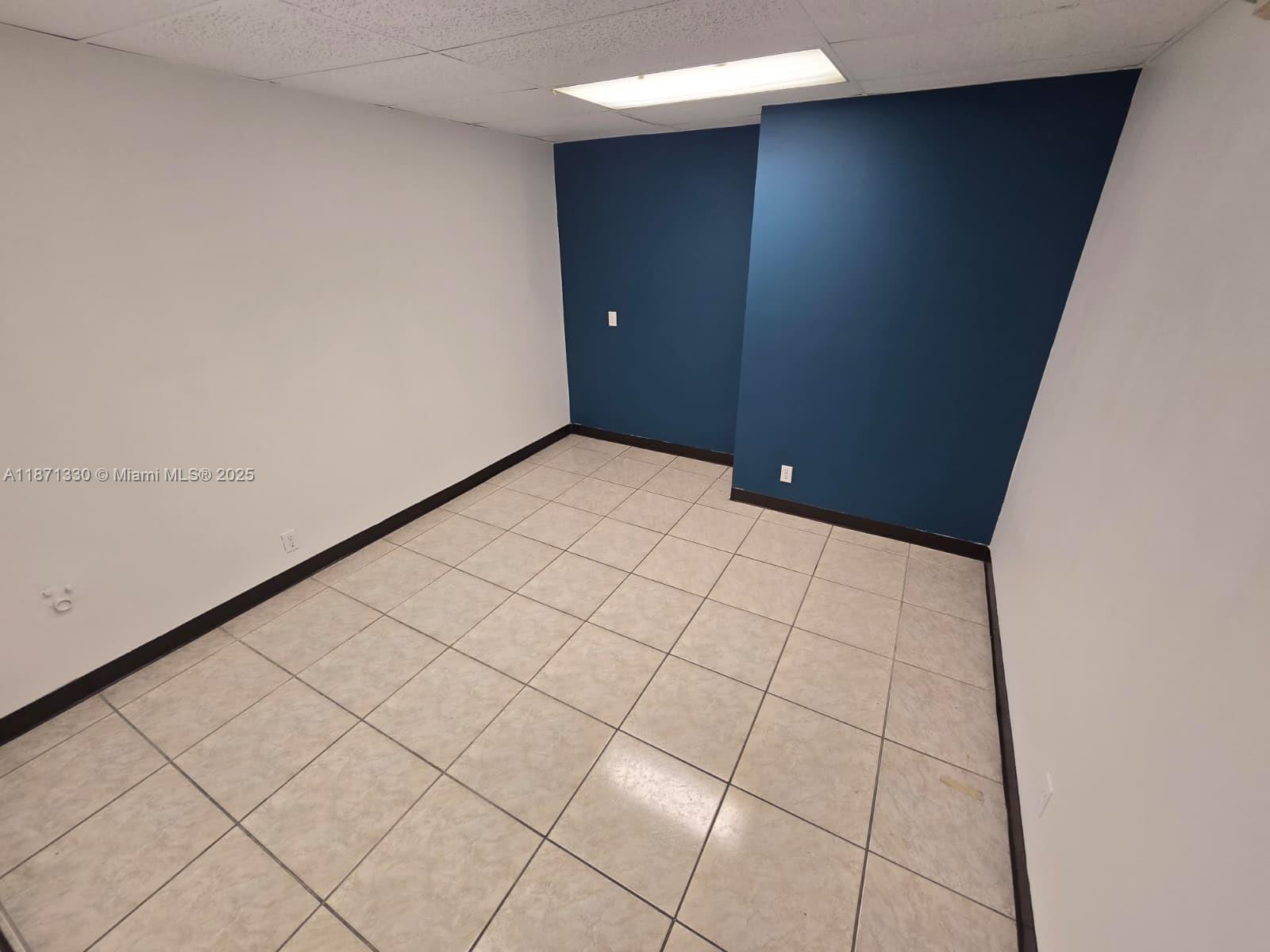 An empty room features white walls, a blue accent wall, and light-colored tiled flooring — 2501 N State Road 7 # 216, Margate FL 33063, MARGATE, FL