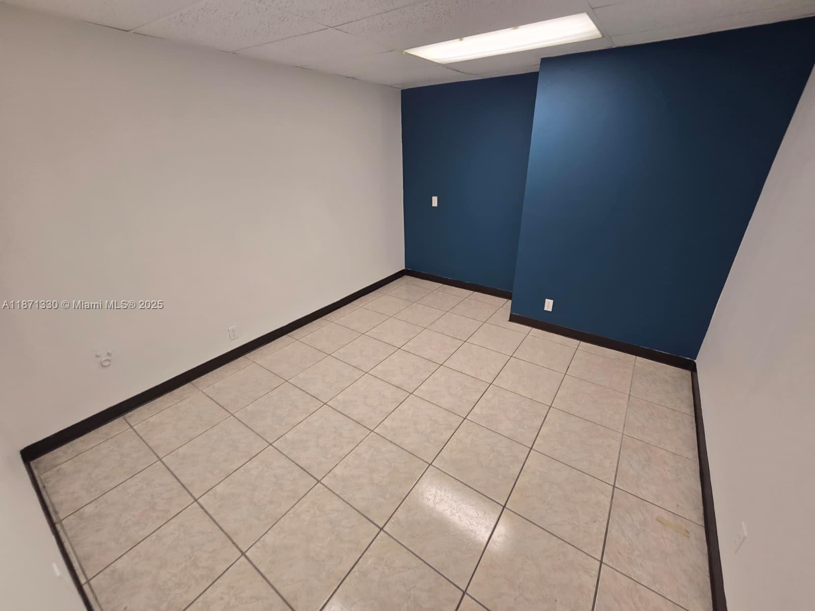An empty room features white walls, a dark blue accent wall, and light-colored tiled flooring — 2501 N State Road 7 # 216, Margate FL 33063, MARGATE, FL