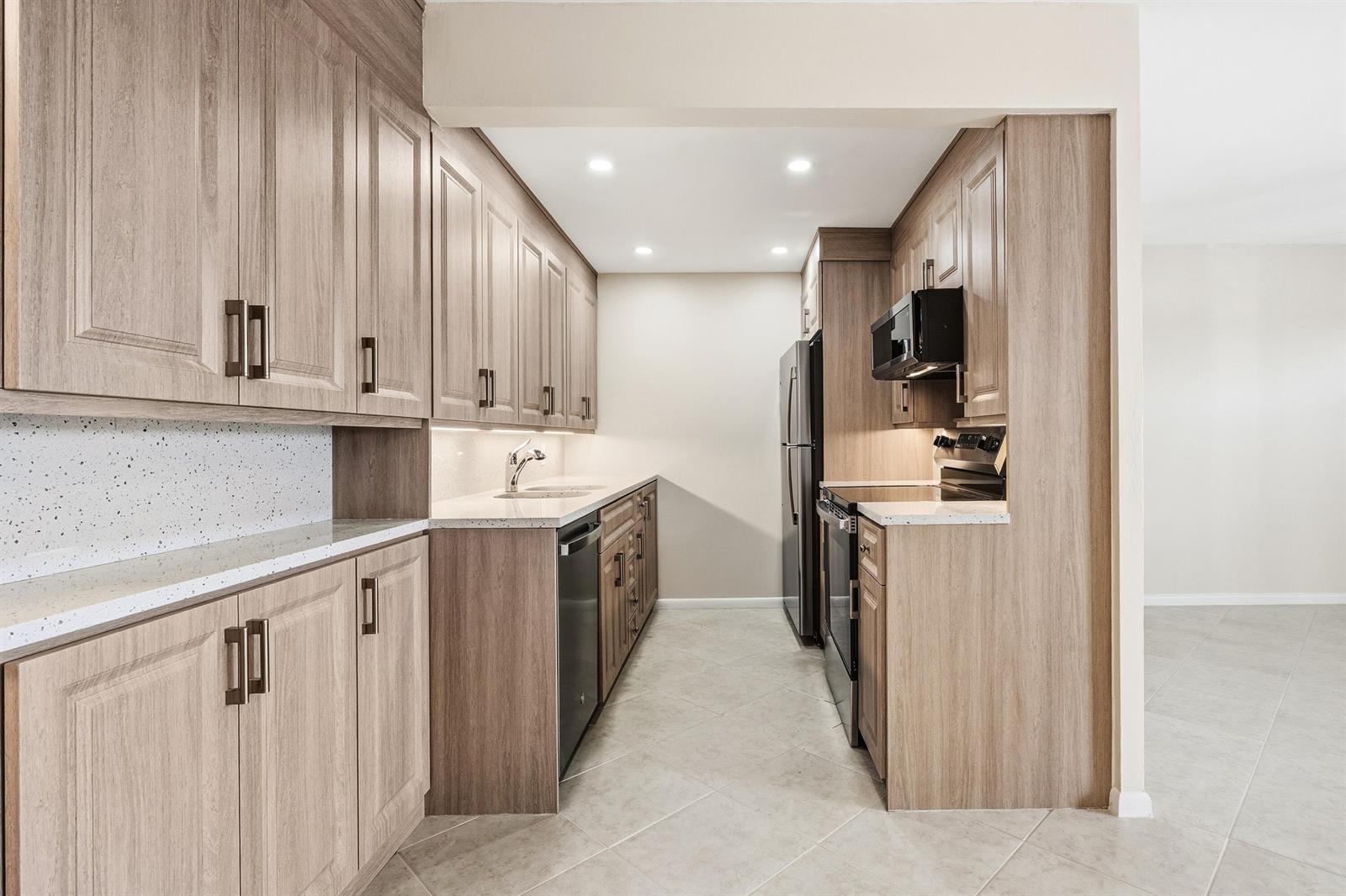A galley kitchen features light wood cabinets, white speckled countertops, and stainless steel appliances — 4067 Yarmouth D, Boca Raton FL 33434, BOCA RATON, FL