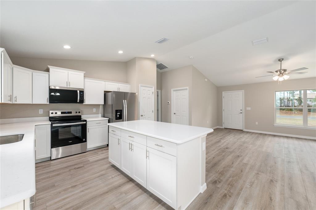 A kitchen with white cabinets, stainless steel appliances, a center island, and light wood flooring — 13 PECAN PASS TRAIL, OCALA, FL