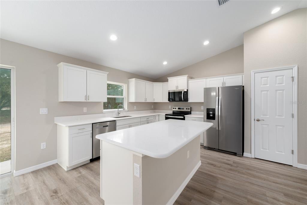 A modern kitchen features white cabinets, a central island, stainless steel appliances, and wood-look flooring — 13 PECAN PASS TRAIL, OCALA, FL