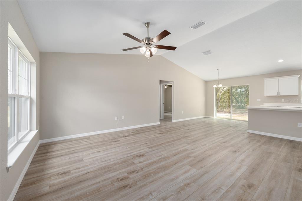 An open-concept living area features light wood-look flooring, a vaulted ceiling, and a ceiling fan — 13 PECAN PASS TRAIL, OCALA, FL