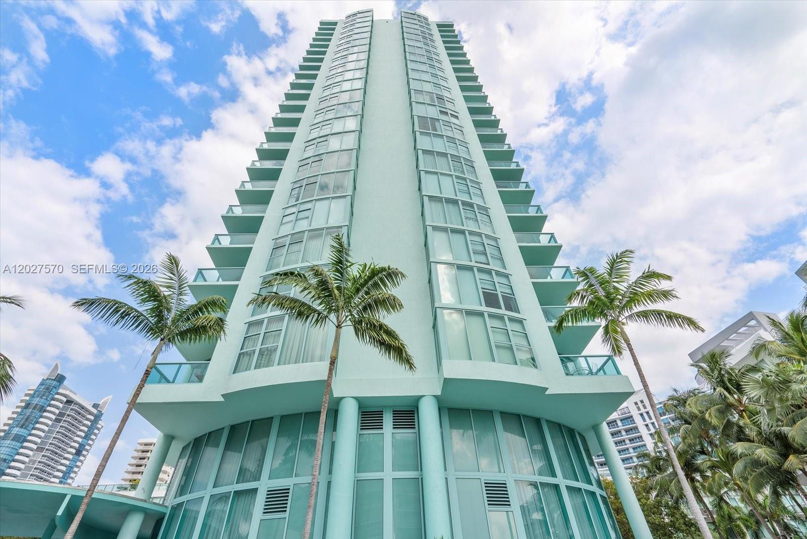 A tall, light-blue residential high-rise building features glass balconies and palm trees in front — 6000 Indian Creek Dr # 8B, Miami Beach FL 33140, MIAMI BEACH, FL