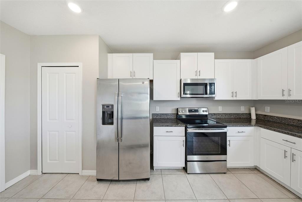 A kitchen features white cabinets, stainless steel appliances, and dark granite countertops over tiled floors — 15617 CHARR ISLAND STREET, SUN CITY CENTER, FL
