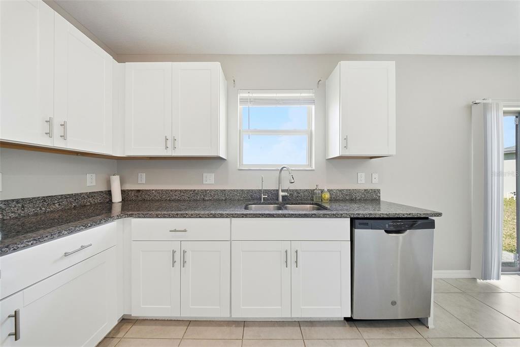 A kitchen with white cabinets, granite countertops, a stainless steel dishwasher, and a window — 15617 CHARR ISLAND STREET, SUN CITY CENTER, FL