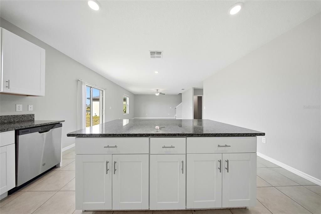 A kitchen island with a dark granite countertop sits in front of white cabinets — 15617 CHARR ISLAND STREET, SUN CITY CENTER, FL