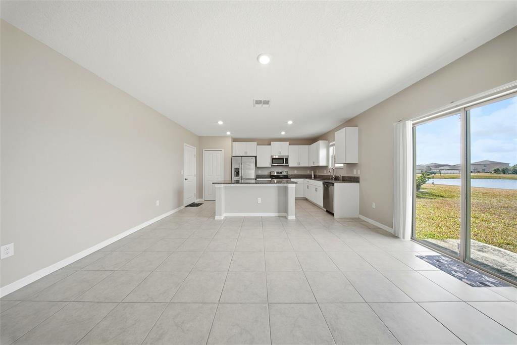 An open-concept kitchen with white cabinets and tile flooring overlooks a backyard pond — 15617 CHARR ISLAND STREET, SUN CITY CENTER, FL