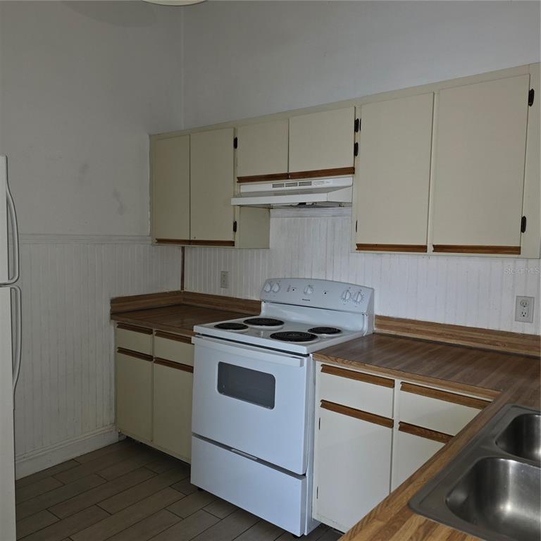 A kitchen features white cabinets, a white electric stove, and wood-look laminate countertops — 6031 SCOTCHWOOD GLEN UNIT 204, ORLANDO, FL
