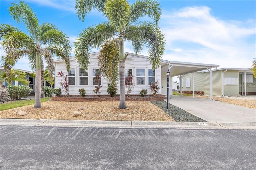 A white manufactured home features a palm tree, a gravel front yard, and a carport — 15550 BURNT STORE ROAD UNIT 87, PUNTA GORDA, FL