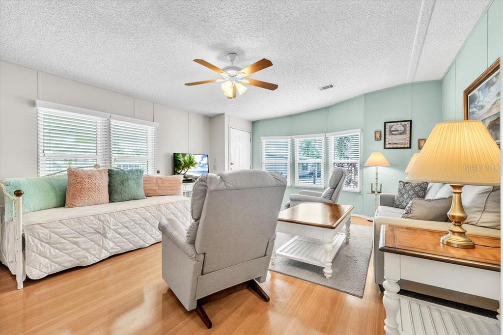 A living room features light wood flooring, a ceiling fan, and a light blue wall — 15550 BURNT STORE ROAD UNIT 87, PUNTA GORDA, FL