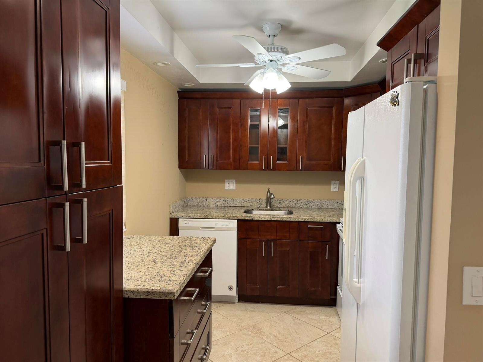 A kitchen features dark wood cabinets, granite countertops, a white dishwasher, and a ceiling fan — 119 Burgundy C, Delray Beach FL 33484, DELRAY BEACH, FL