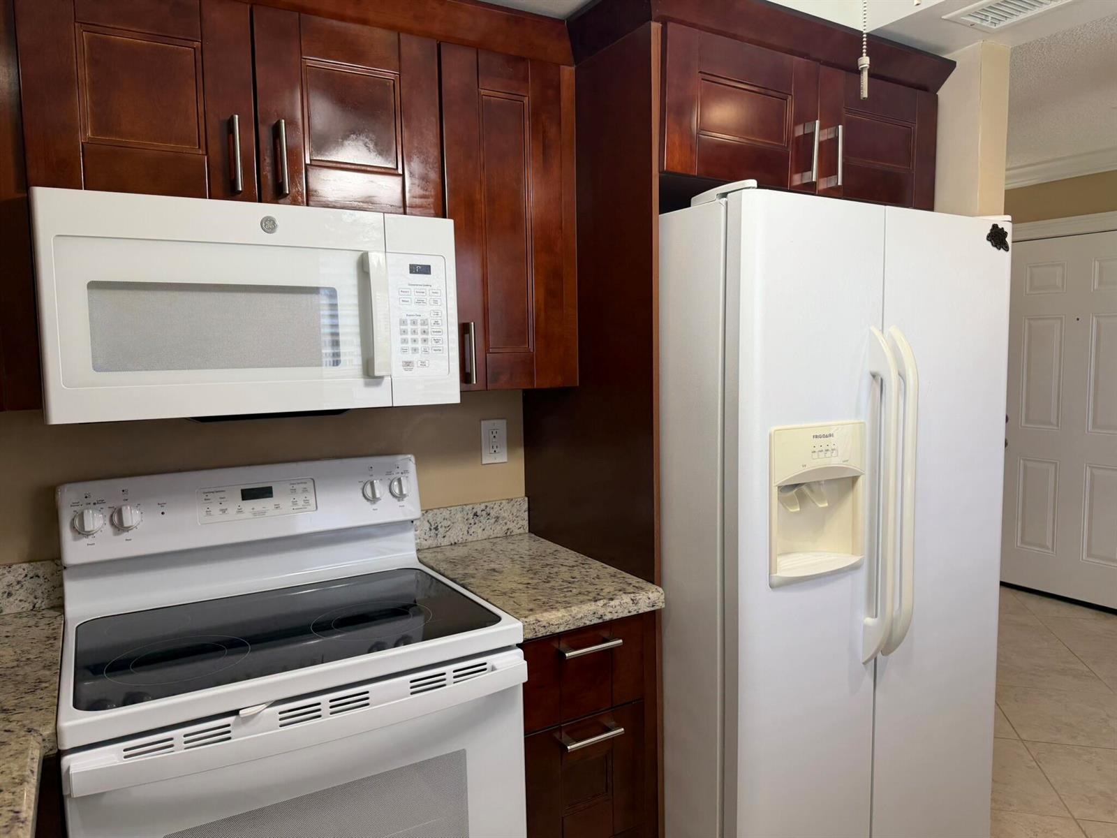 A kitchen featuring dark wood cabinets, white appliances, and granite countertops — 119 Burgundy C, Delray Beach FL 33484, DELRAY BEACH, FL