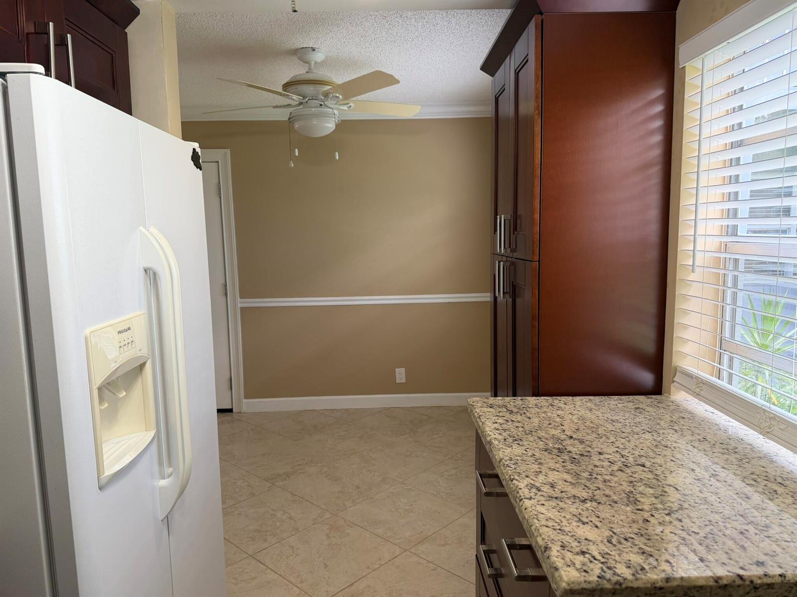A kitchen area with a white refrigerator, dark wood cabinets, granite countertops, and tile flooring — 119 Burgundy C, Delray Beach FL 33484, DELRAY BEACH, FL