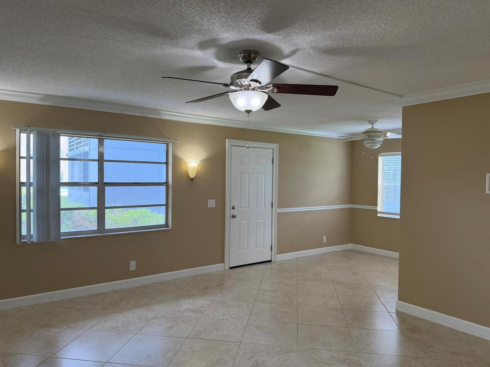 An empty room with tan walls, tile flooring, a ceiling fan, and a white door — 119 Burgundy C, Delray Beach FL 33484, DELRAY BEACH, FL