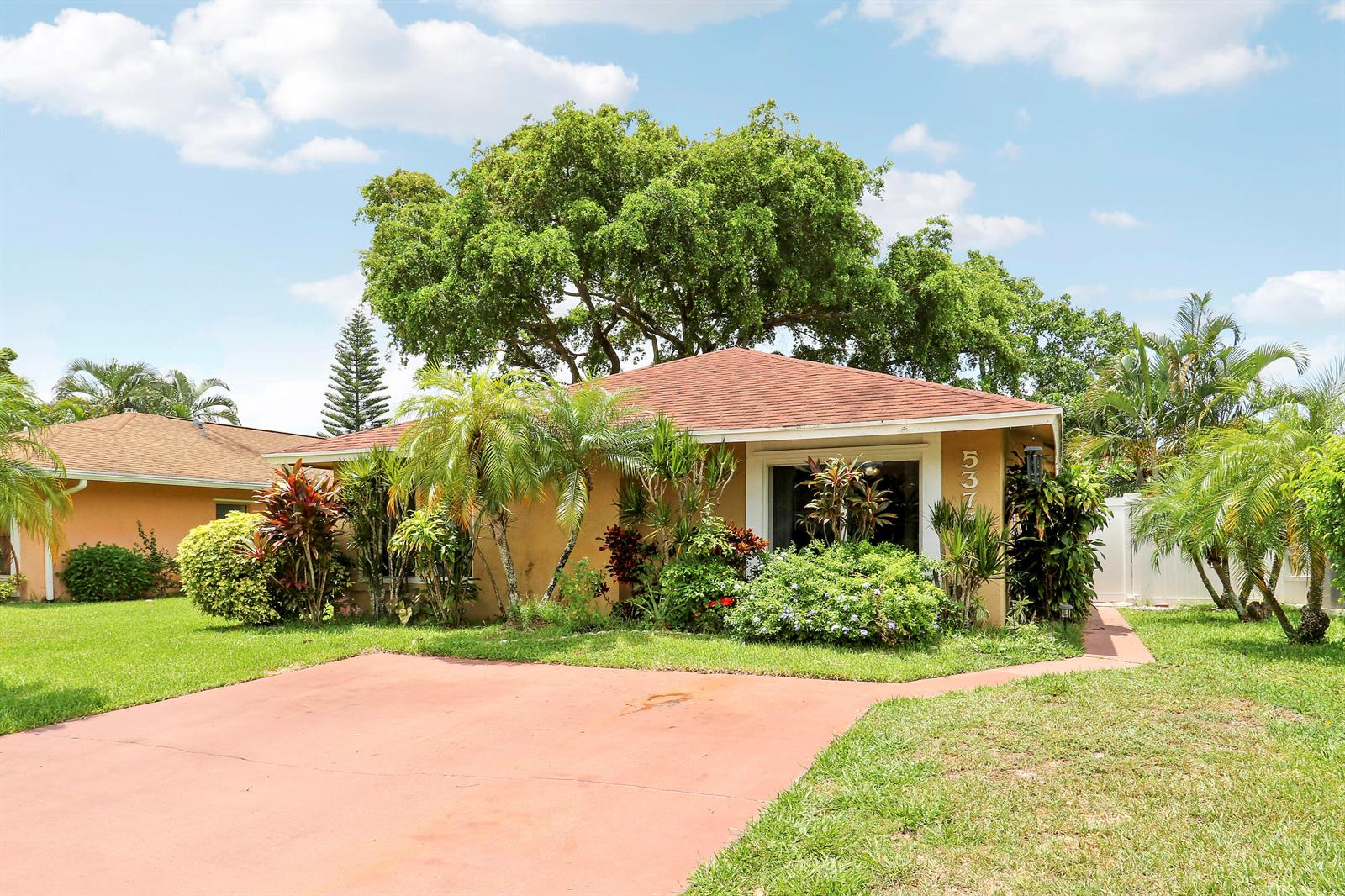 A single-story house with a red roof, tan exterior, and lush landscaping sits behind a driveway — 5373 Gene Circle, West Palm Beach FL 33415, WEST PALM BEACH, FL